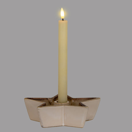 Hill Interiors Small Cement Star Candle Holder in white, holding a single lit ivory taper candle, shown against a plain grey background.