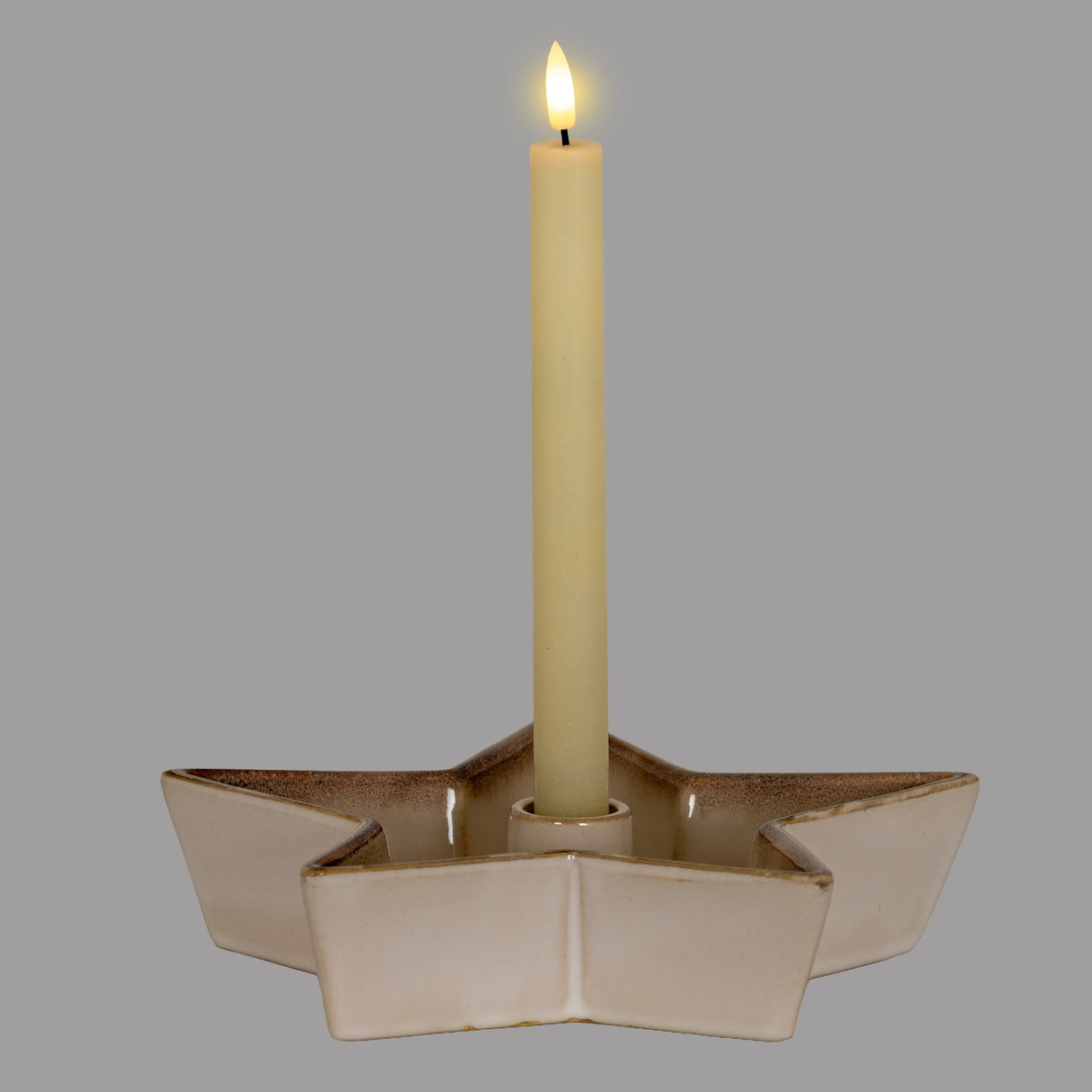 Hill Interiors large ceramic star candle holder in white with a soft glazed finish, holding a lit taper candle at its centre against a grey background.