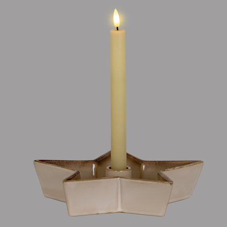 Hill Interiors large ceramic star candle holder in white with a soft glazed finish, holding a lit taper candle at its centre against a grey background.