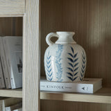 Hill Interiors Blue Floral Amphora Jug Vase in white crackle-glazed ceramic with blue leaf motif and small handle, on a book atop a wooden shelf.