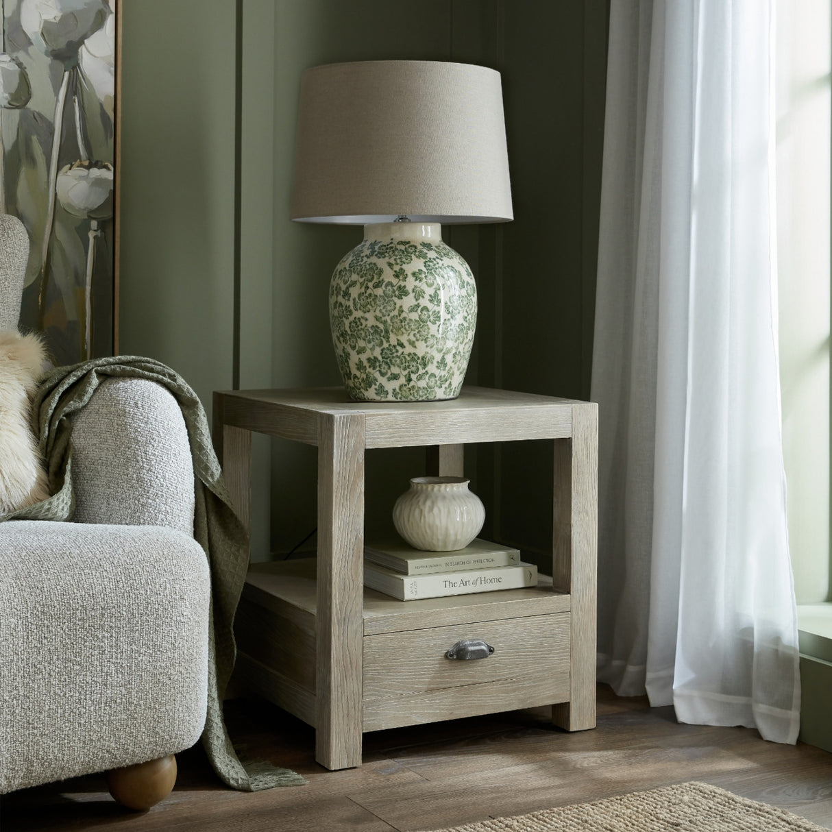 Hill Interiors Ceramic Pot Table Lamp with green floral glaze and neutral drum shade, styled on a light oak side table in a green living room.