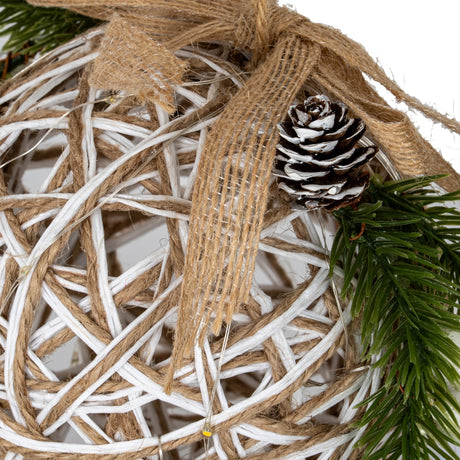 Close-up of the Hill Interiors small LED white rattan-effect bauble showing woven plastic strands, jute ribbon, a frosted pinecone and green pine sprig.