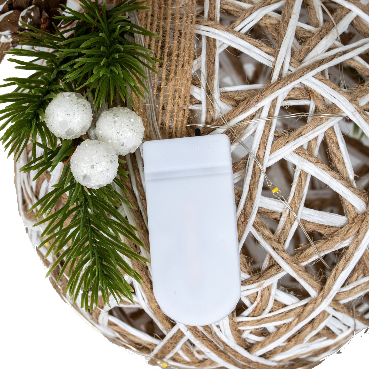 Close-up of Hill Interiors small LED white rattan-effect bauble showing the woven frame, battery unit, warm LED wire and pine sprig with white berries.