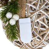 Close-up of Hill Interiors small LED white rattan-effect bauble showing the woven frame, battery unit, warm LED wire and pine sprig with white berries.