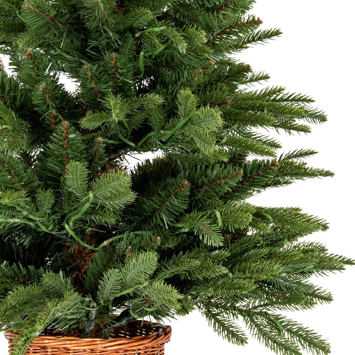 Close-up of Hill Interiors Pre-Lit LED Fir Tree showing dense green plastic branches with integrated warm LED string lights set in a woven rattan pot.