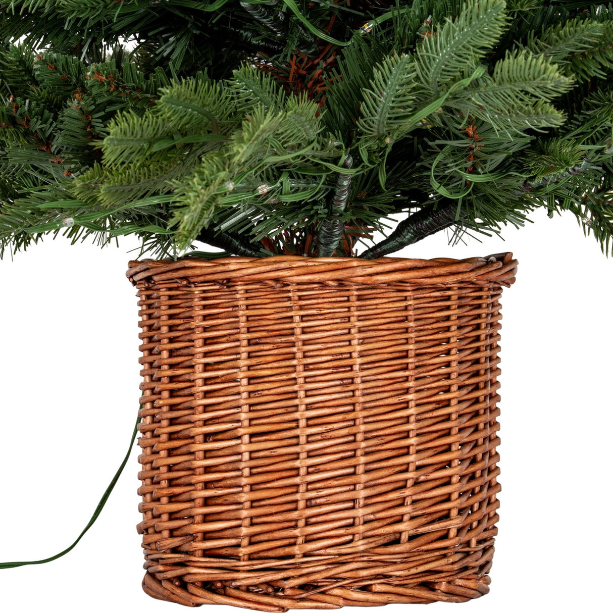Close-up of the Hill Interiors Pre-Lit LED Fir Tree base showing green plastic branches set in a woven rattan pot on a plain white background.