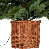 Close-up of the Hill Interiors Pre-Lit LED Fir Tree base showing green plastic branches set in a woven rattan pot on a plain white background.