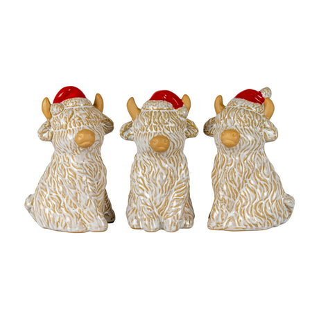 Three Hill Interiors white ceramic Highland cow ornaments with shaggy textured coats, tan horns and noses, wearing red Santa hats on a white background.