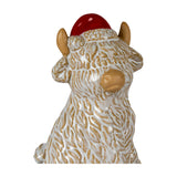 Hill Interiors ceramic highland cow ornament in white with tan horns, nose and shaggy coat detailing, wearing a red Santa hat, on a white background.