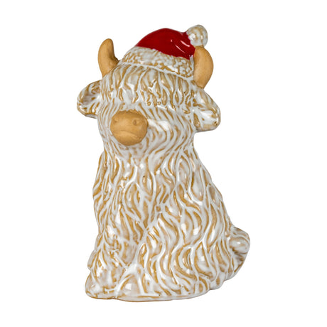 Hill Interiors ceramic Highland cow ornament in white glaze with tan horns, nose and ears, wearing a red Santa hat, on a plain white background.