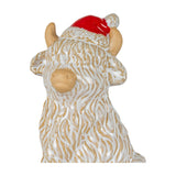 Hill Interiors ceramic highland cow ornament in white glaze with sandy horns, ears and muzzle, wearing a red Santa hat, on a white background.