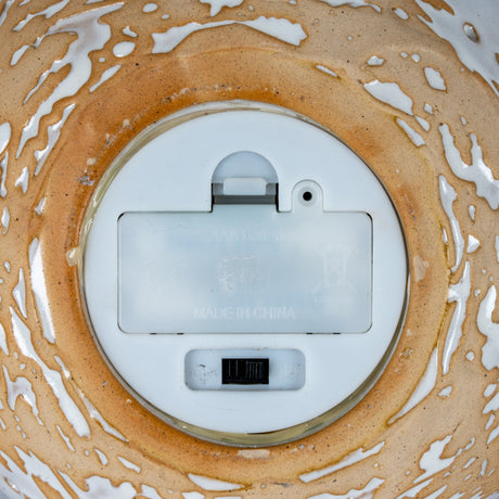 Underside of Hill Interiors ceramic snowman showing white battery compartment with on/off switch, set within the tan and white drip-glazed base.