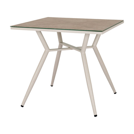 Hill Interiors square side table with a beige glass top and slim tapered cream metal legs joined by a cross stretcher, on a plain white background.
