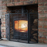 Hill Interiors Heavy Large Ornate Fire Screen in black metal with scrolled detailing, set on a stone hearth before a lit fire in a brick fireplace.