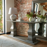Hill Interiors cream stone woman's head sculpture displayed on a grey pedestal console table with a lamp and books against an exposed brick wall.