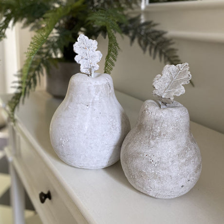 Hill Interiors Stone Pear Decorative Ornament in beige, shown as two matte stone pears with textured leaf stems on a cream console beside ferns.