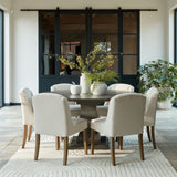 Hill Interiors Stone Decorative Apple in beige sits on a round wood dining table with boucle chairs, vases of foliage and dark framed doors behind.