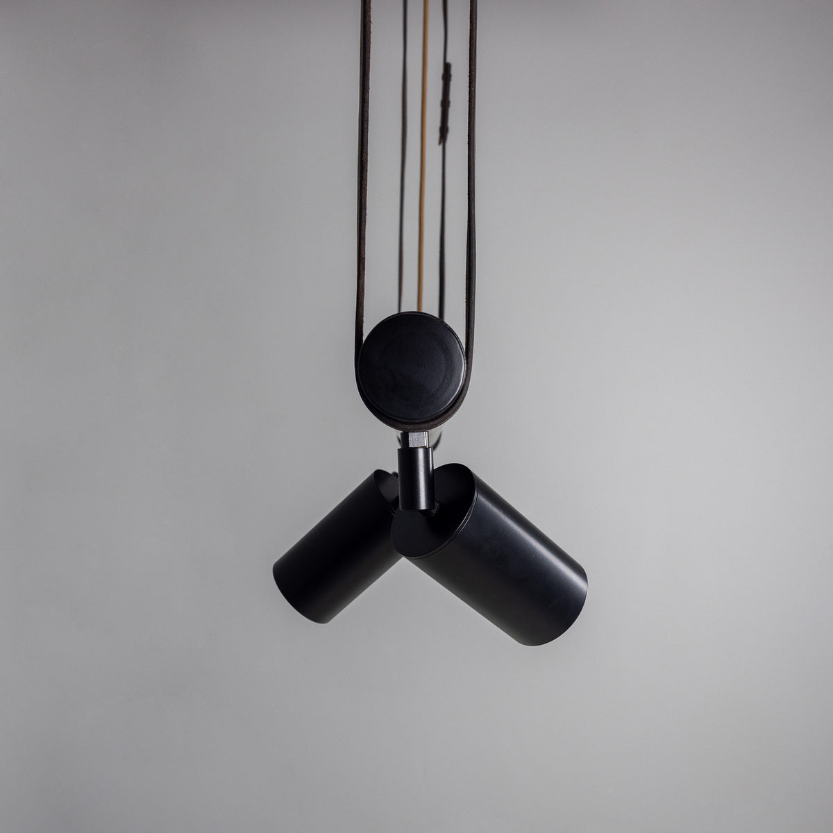Holmes Brass 5 Light Spotlight Bar in matt black, two cylindrical spot heads shown suspended from leather straps with a round ceiling mount against a plain grey background.