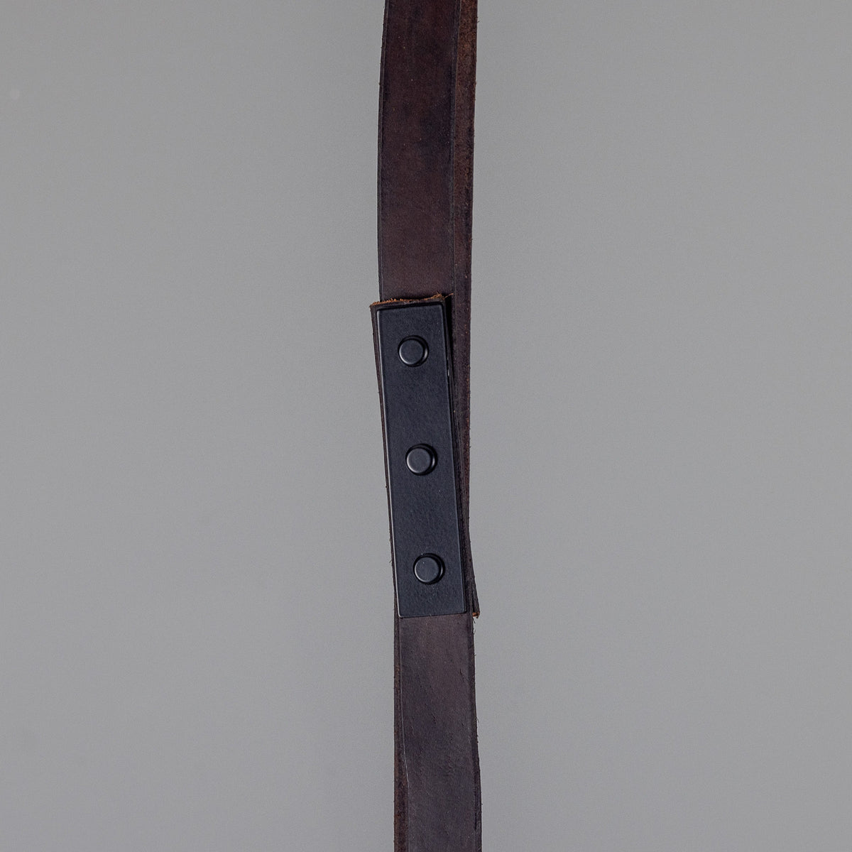 Close-up of the Holmes Brass 5 Light Spotlight Bar showing a dark leather hanging strap with riveted metal bracket against a plain grey background.