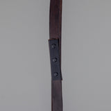 Close-up of the Holmes Brass 5 Light Spotlight Bar showing a dark leather hanging strap with riveted metal bracket against a plain grey background.