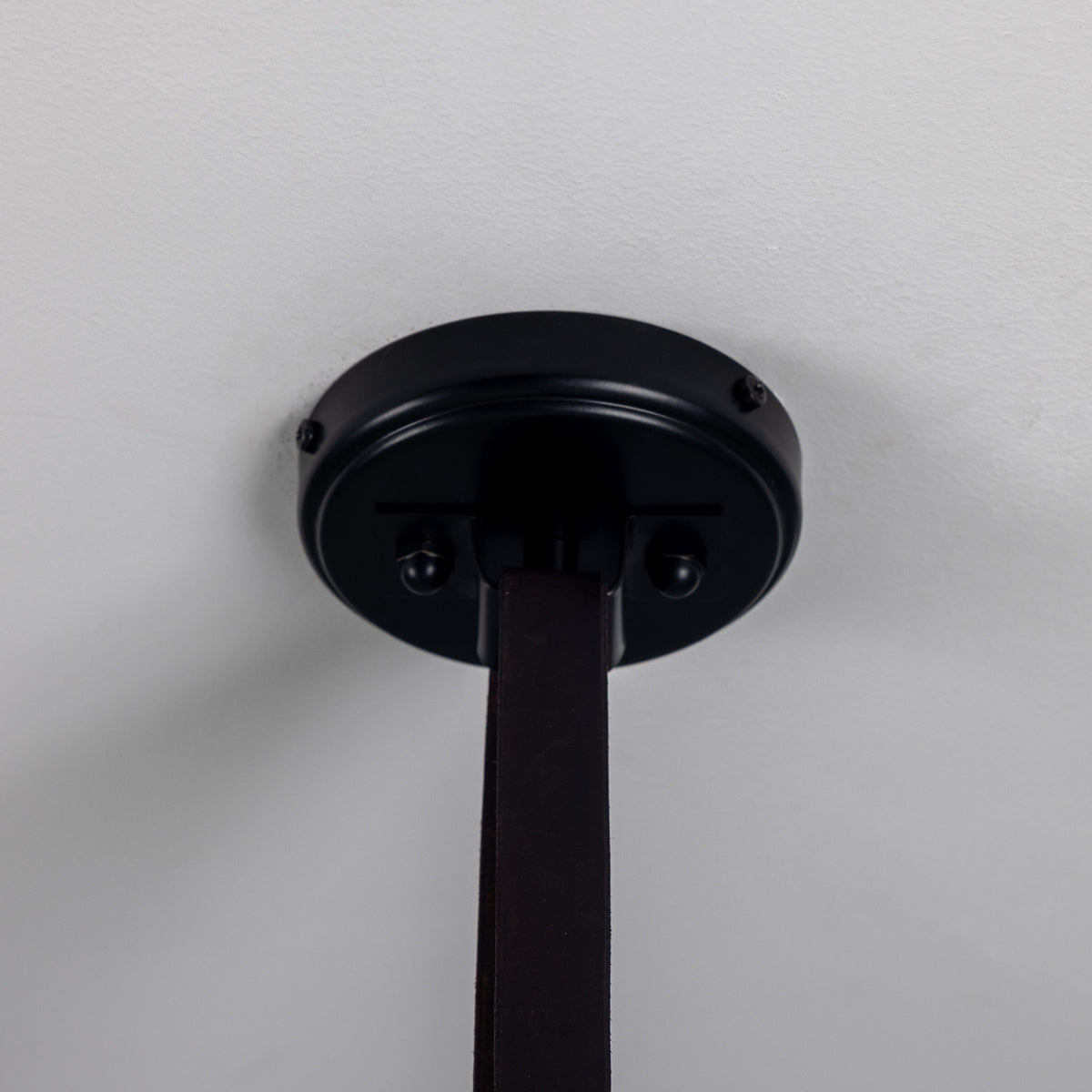 Close-up of the Holmes 5 Light Spotlight Bar's matt black ceiling canopy with leather strap suspension, set against a plain light background.