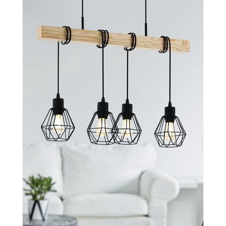 Hosmane 4 Light Linear Pendant Light in black steel with a natural wood beam, four faceted wire cage shades on black flex cords, shown above a white sofa in a living room.
