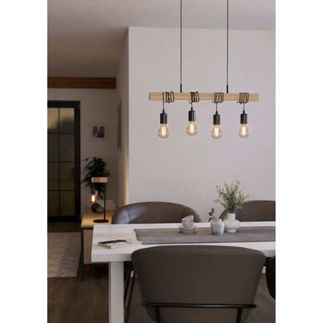 Hosmane 4 Light Linear Pendant Light in black and wood, shown over a dining table with exposed bulbs and coiled black cables along the wood beam.