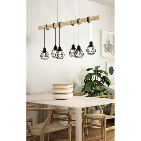 Hosmane 6 Light Linear Pendant Light in black, featuring wire-cage shades hung from a natural wood beam, shown above a dining table in a bright room.