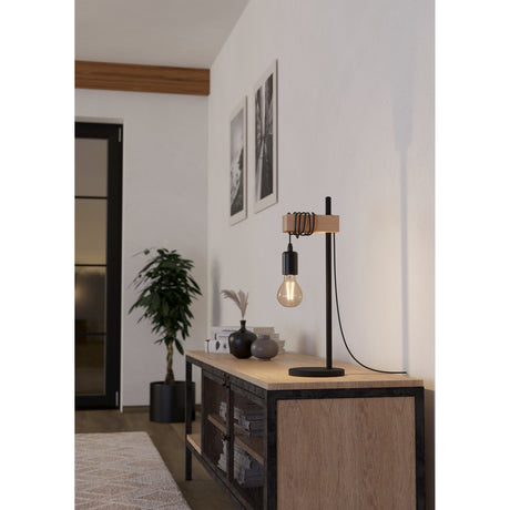 Hosmane Table Lamp in black steel and pale wood, round base, slim upright with wooden crossbar and looped cable, exposed bulb, shown on a sideboard in a living room.
