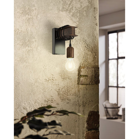 Hosmane Wall Light in black and brown, with a steel I-beam backplate and black cord dropping to an exposed E27 bulb, mounted on a textured plaster wall.