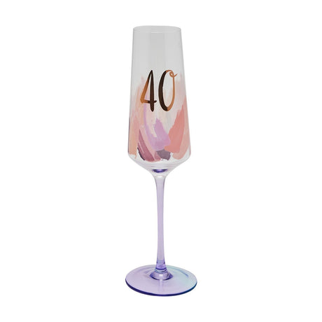 Glass champagne flute with "40" in metallic gold over pink and lilac brushstrokes on the clear tapered bowl, set on a lilac stem and foot, shown against a plain white background.