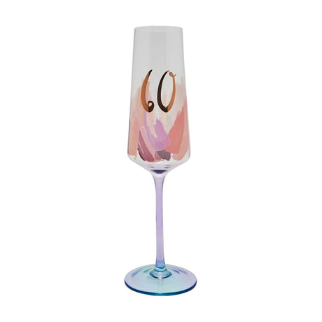 Clear glass champagne flute with a "60" in gold script above pink and peach brushstroke detailing, a slender lilac stem, and a round blue-tinted foot, shown on a white background.