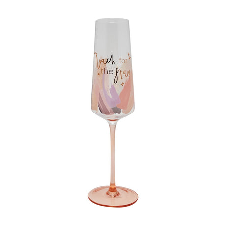 Champagne flute with clear tapered bowl reading "Reach for the Stars" in script, pastel pink, peach and lilac brushstroke design, tinted pink stem and round foot, on a plain white background.