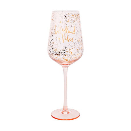 Stemmed wine glass with pale pink bowl and rose-gold speckled finish, gold "Weekend Vibes" script, slim pink stem and round foot, shown on a plain white background.