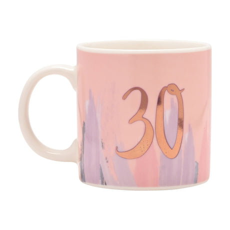 Porcelain 30th birthday mug with blush pink body, watercolour-style lilac and grey brushstrokes, cream handle, and a gold script "30" on one side, shown on a white background.