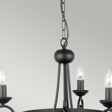 Close-up of the Harlech 3 Light Chandelier - Black, highlighting its medieval design with three candle-style lights. The bulbs cast a warm glow against a simple light gray background.