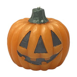 Round orange pumpkin candle, 7cm, with debossed black jack-o'-lantern face and a dark green stem wick, shown on a plain white background.