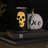 Round black LED lantern, 15.2cm, with a glowing gold skull silhouette design, displayed on books beside a white "boo" pumpkin in a Halloween setting.