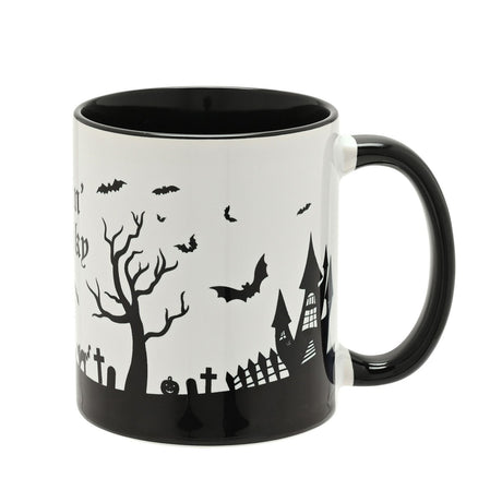 Feelin' Spooky stoneware mug with black handle and rim, white glazed body showing bats, bare trees, a haunted house, and gravestones in black silhouette, on a plain white background.