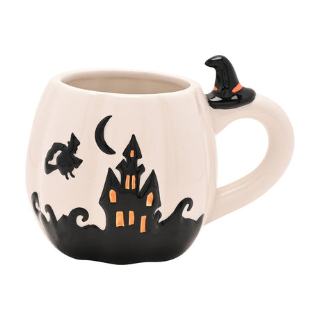 Pumpkin-shaped white stoneware mug with black haunted house, crescent moon, and witch design, plus a tiny witch's hat at the handle, on a plain background.
