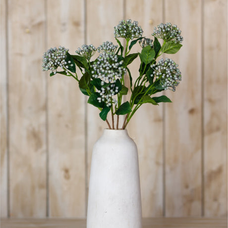 Hill Interiors Blue Budding Hydrangea Spray artificial stems with clustered blue-grey buds and green leaves arranged in a white ceramic vase against light wood.