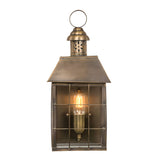 The Hyde 1 Light Outdoor Wall Light in Aged Brass offers a vintage touch with its glass cover and grid pattern. It emits a warm glow when illuminated and includes a loop on top for hanging, bringing timeless charm to any setting.