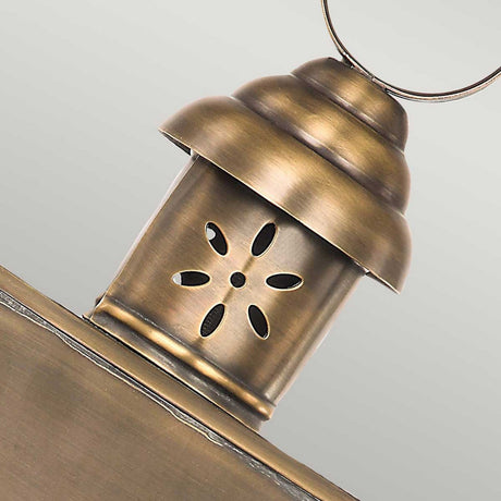 A close-up of the Hyde 1 Light Outdoor Wall Light in aged brass highlights its vintage appeal. This wall light features a vented top with a circular pattern of cutouts for ventilation and a loop handle at the top, while its antique finish adds to its timeless charm.