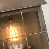 A close-up of the illuminated Hyde 1 Light Outdoor Wall Light in its metal cage fixture captures its undeniable vintage appeal. The light casts a warm glow, while the rusty brushed metal frame, with intersecting vertical and horizontal bars, evokes the charm of an aged brass lantern.