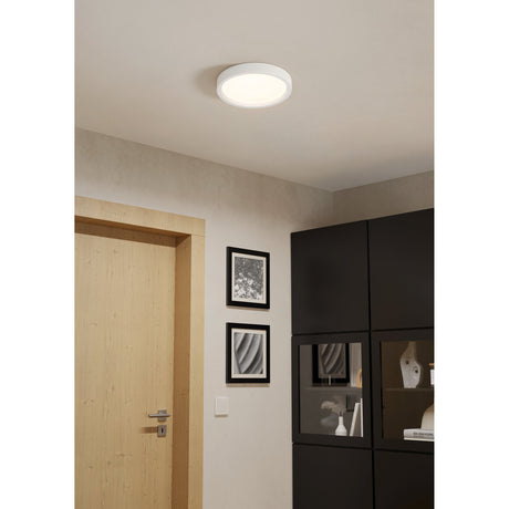 Idun-E LED flush ceiling light, round white plastic fixture with frosted diffuser, 28.5cm, warm white light, shown on a hallway ceiling near a wooden door and dark cabinets.