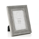 Grey embossed wood-effect photo frame with wide stepped moulding and rear easel stand, shown at an angle on a plain white background, holds a 4 x 6" photo.