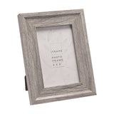 Rectangular 4x6" photo frame with embossed wood-effect grey finish and wide stepped moulding, shown at an angle on its fold-out easel stand against a white background.