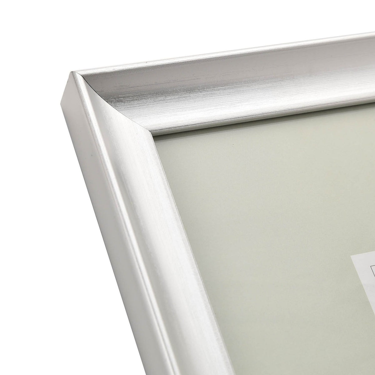 Close-up of a rectangular photo frame's mitred corner in brushed silver finish, showing sloped moulding with visible grain lines, on a plain white background.