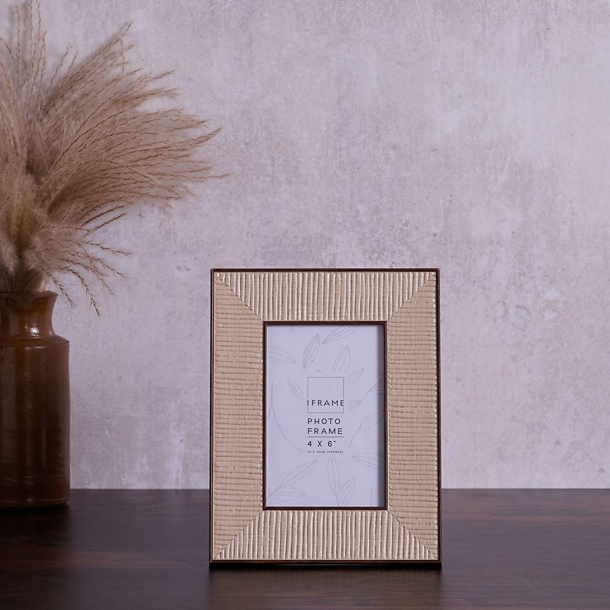 Rattan effect 4x6" photo frame with stand in natural woven texture and dark brown edging, shown on a dark wood surface against a neutral wall.