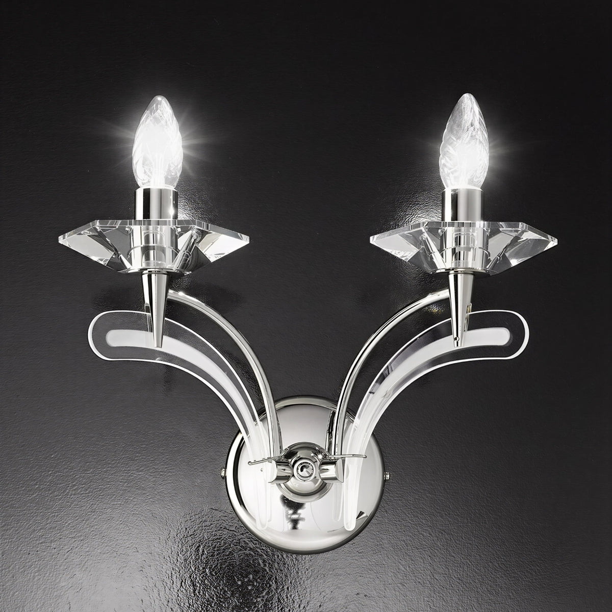 Icaro 2 Light Glass Wall Light in chrome finish with two upward-curved arms, crystal-effect glass drip pans and lit candle-style bulbs, shown against a dark background.